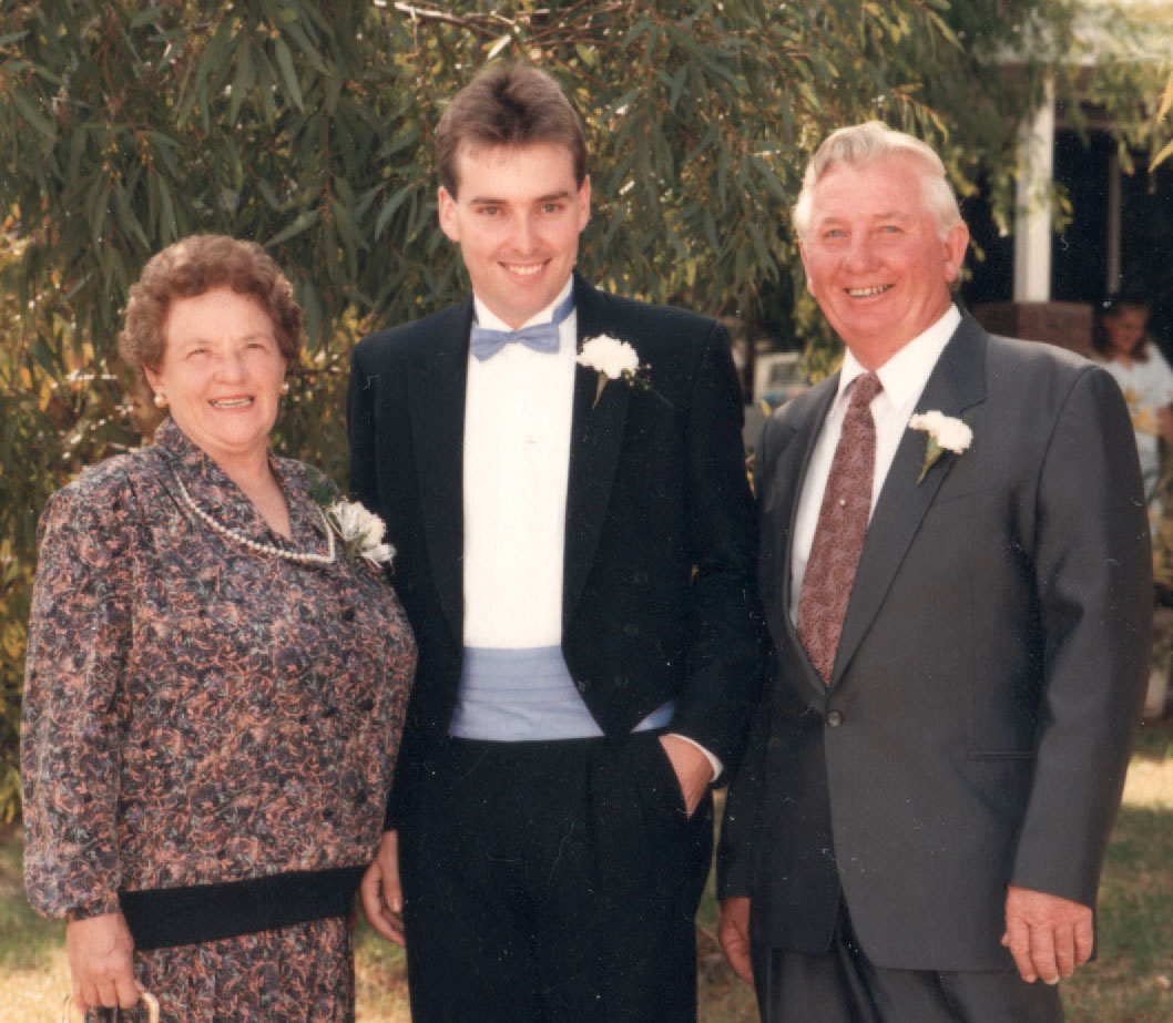 my mother, joyce is wearing a nice necklace and holding a bag, and my dad is on the right in a suit, while I am in the middle looking great!