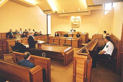 Inside the court at Sir Samuel Way building. Showing a judge, with three workers in front of him, a few lawyers, a jury, marshall, witnesses and an observer. Court accessibility is bad