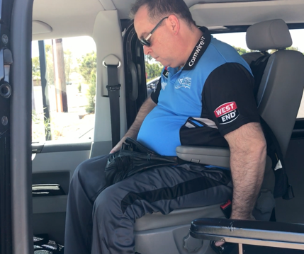 In my van, I am wearing a blue shirt and my left arm is reaching for the control which allows the seat to go up and down, rotate, and move backwards and forwards