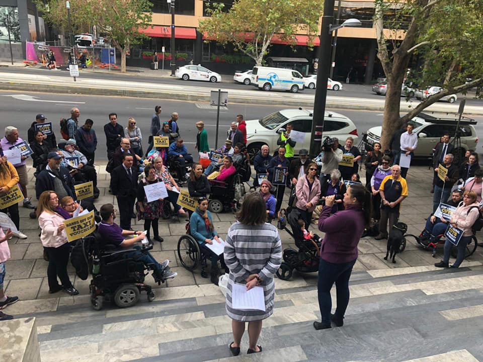 showing many people protesting in front of parliament house. Most are holding signs that support keeping SATSS. Lisa Pierce is addressing the crowd 