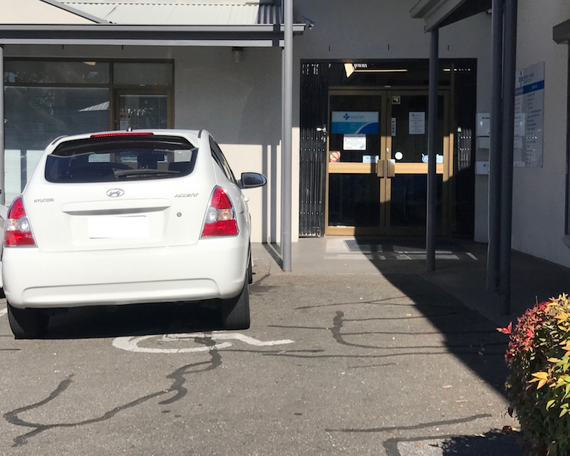 a white car is parked in an accessible parking spot at the doctor's surgery. There is little room for wheelchairs to get in and out of vehicles