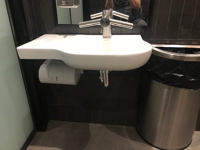 In the bathroom, there is room for legs to go under the white sink. Hands can be washed, and there is a dryer built into the tap. 