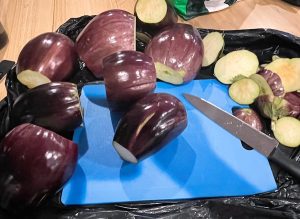10 eggplants with ends chopped off, sitting on a blue plastic cutting board, sitting on a black plastic bag on a wooden table. Tasty Eggplant Soup